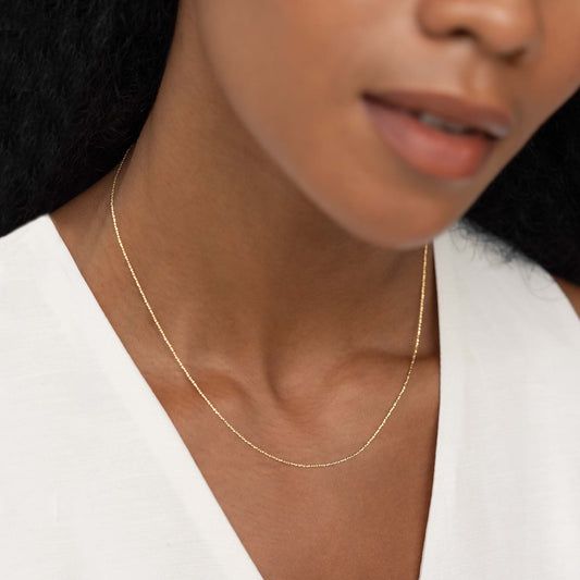 Närbild på en kvinna som bär ett elegant bismarckhalsband i guld.